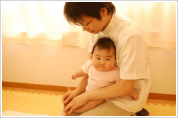 主に布団の上で治療しますが、お父さん、お母さんに抱っこしていただく ことも出来ます。 写真は、足のツボにはりを当てているところです。